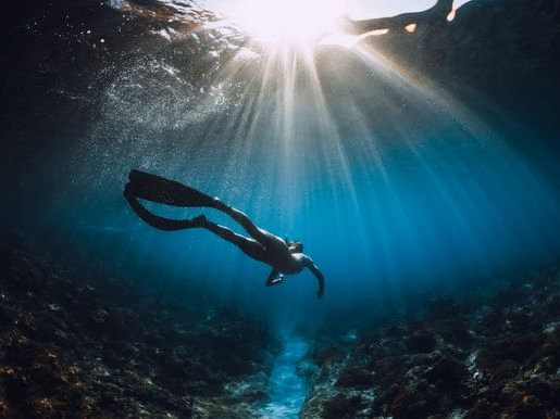 Mujer joven apneista con deslizamientos de aletas y asombrosos rayos de sol. apnea bajo el agua en el mar